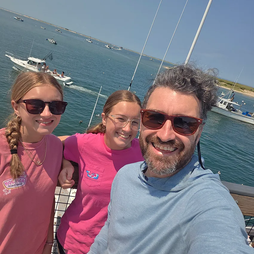 Me and my two daughters on a pier in Chatham, Cape Cod, with boats out on the water behind us.